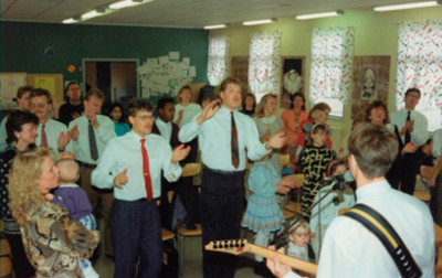 Lovsång och överlåtelse har karaktäriserat församlingen hela tiden. Denna bild är från ett möte i Enåkers Bygdegård i början av 1990-talet. Längst till vänster ser vi Dave & Chris Richards.